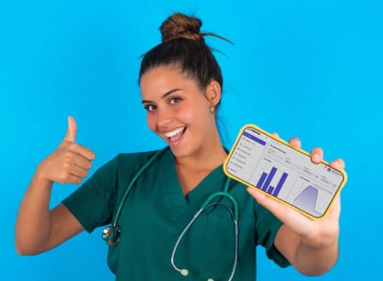 sköterska i grön dräkt på blå bakgrund med en telefon som visar MERIDIQ journalsystem rapportvy